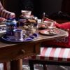 The longest reigning monarch tea set on a wood table. Biscuits are in a dish and on a plate. There is a red cushion on a chair  thumbnail