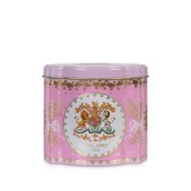 Close up shot of a pink tin tea caddy. At the centre is the Royal Coat of Arms in a white circle and edged with gold. Foliage tied with ribbon and acorns adorn the space.  