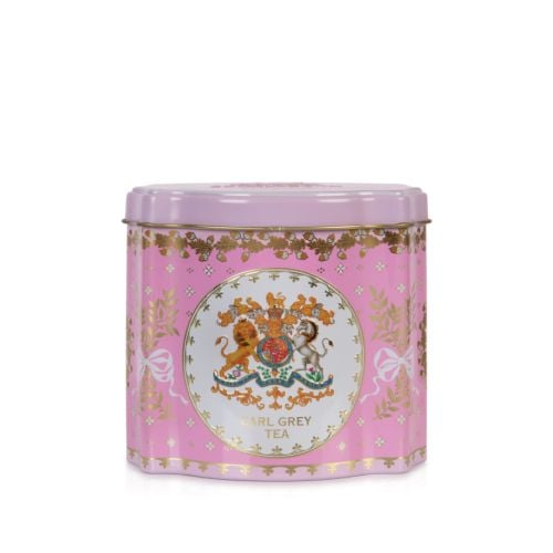 Close up shot of a pink tin tea caddy. At the centre is the Royal Coat of Arms in a white circle and edged with gold. Foliage tied with ribbon and acorns adorn the space.  