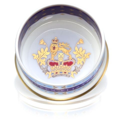 This pillbox has a lid with the lion and unicorn crest. The edge of the pillbox is gold, light blue and purple design. HM Queen Elizabeth reads on the edge of the pillbox