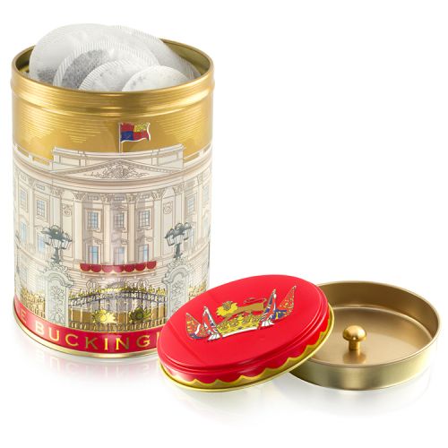 Gold tea caddy with lid off. Round teabags inside. Red lid with lion on a crown and flags surrounding. The main body of the tea caddy has the Buckingham Palace facade wrapped around. 