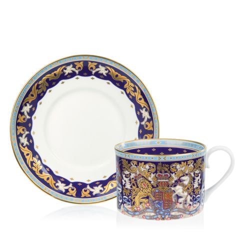 The longest reigning monarch teacup and saucer. The saucer is stood behind the cup. With a white centre and a purple, gold and light blue edge. The cup is purple, light blue and gold with the lion and unicorn crest at the centre.