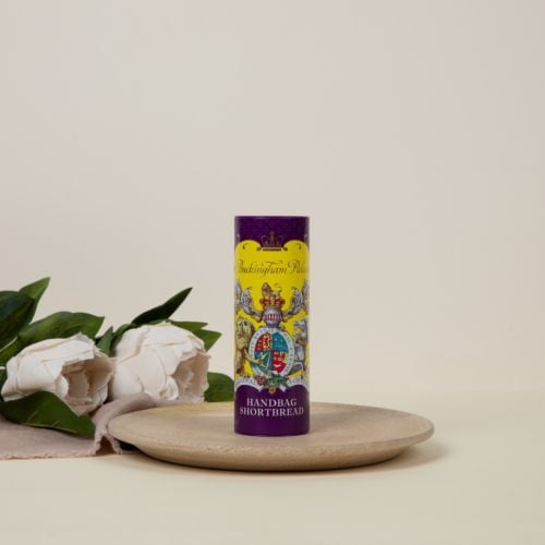 Miniature shortbread biscuit tube featuring a yellow and purple design. At the centre of the design is the coat of arms including a lion and unicorn. Next to the tube of biscuits are two shortbread rounds