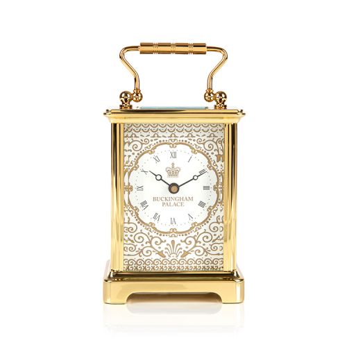 Gold carriage clock with an elaborate pattern and the words 'Buckingham Palace' on the face with a crown.