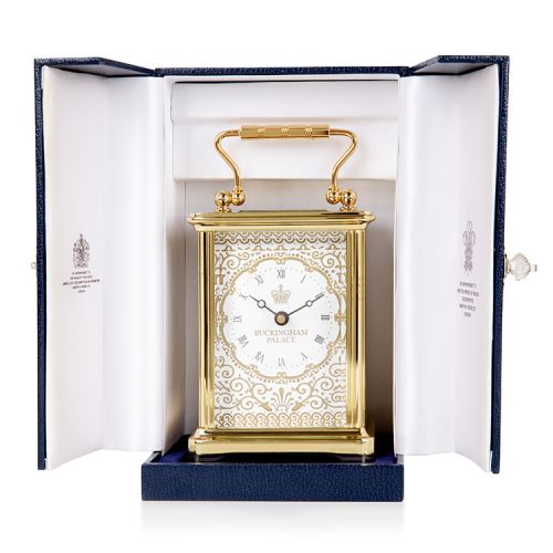 Gold carriage clock with an elaborate pattern and the words 'Buckingham Palace' on the face with a crown.