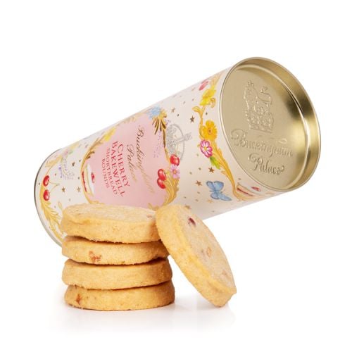 A cardboard tube of cherry bakewell biscuits. There is a floral garland at the top and bottom of the tube. At the centre of the tube is a pink oval reading the words 'Buckingham Palace' in gold and 'cherry bakewell shortbread rounds' in red. The oval is s