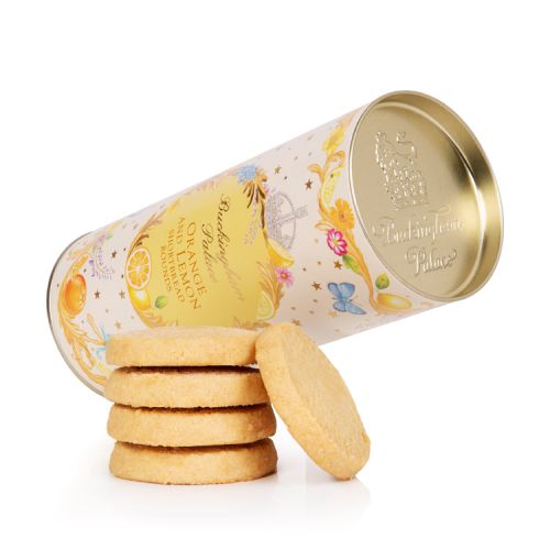 A cardboard tube of orange and lemon biscuits. There is a floral garland at the top and bottom of the tube. At the centre of the tube is an orange oval reading the words 'Buckingham Palace' in gold and 'Orange and lemon shortbread rounds' in orange.