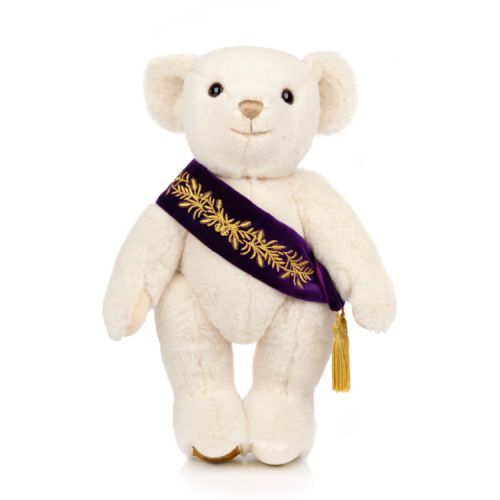 Merrythought teddy bear with a purple sash embroidered with gold leaf pattern and a gold tassel.