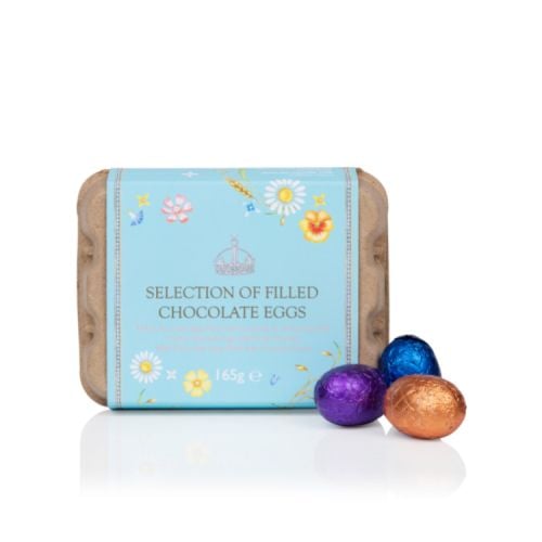 Cardboard egg box with a blue floral wrap band. Next to the box are three chocolate foiled eggs wrapped in purple, blue and orange foils.