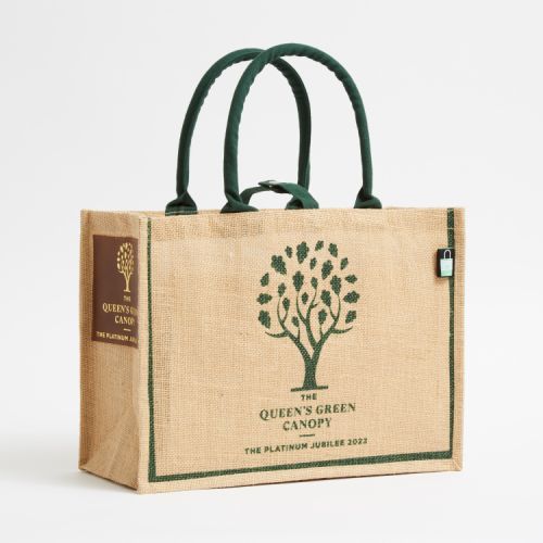 Brown juco bag printed with a green tree and the words 'The Queen's Green Canopy The Platinum Jubilee 2022.' The bag has green handles and a leather label on the side