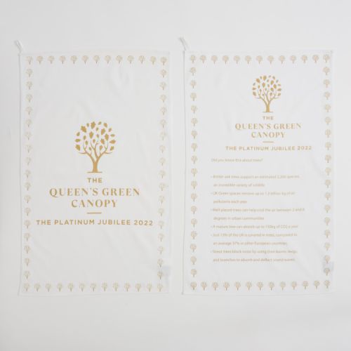 Front and reverse of The Queen's Green Canopy tea towel. The front of the tea towel has a gold tree and the logo and on the reverse it is a list of tree facts