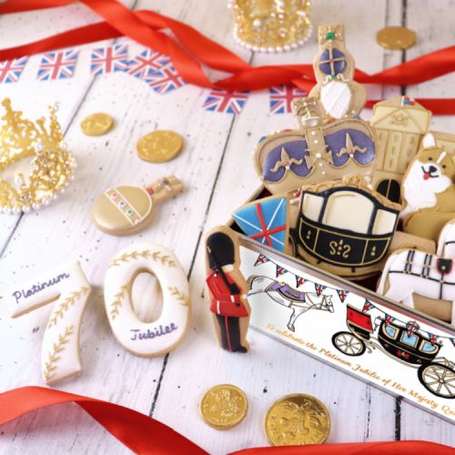 A selection of iced biscuits including carriages, the façade of Buckingham Palace, guardsmen and corgis. They are in an illustrated tin, decorated with corgis, carriages and 70. 