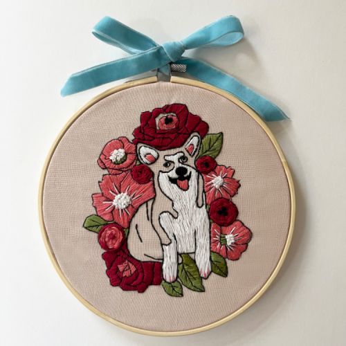 Round embroidery hoop embroidered with a corgi and flowers and tied with a blue velvet ribbon