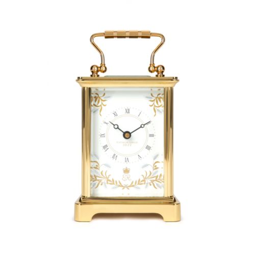 Gold carriage clock with a white background and gold handle. There is a clock face surrounded by the design of wheat ears and olive branches. On the clock face are the words 'Platinum Jubilee 2022' and an ER surmounted by the crown.