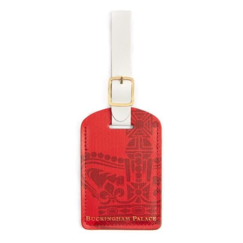 Luggage tag in red with white buckle and decorative crown and the words Buckingham Palace on the bottom of the tag in gold