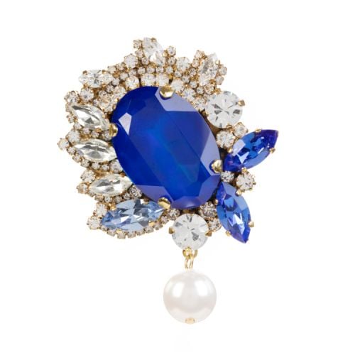 Gold brooch with large central blue crystal, surrounded by varying size and shapes of clear crystals. Finished with a pearl drop.