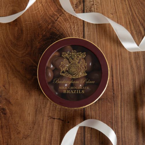 Lid of chocolate brazil nut box with view to inside of packaging with the chocolate brazil nuts seen. wording with the buckingham palace crest in gold foil and maroon lining.