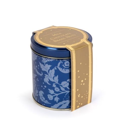 Blue tin with acanthus print and crown embellished lid. A pile of chocolate covered brazil nuts next to the tin. 