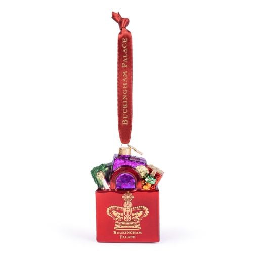 Red Buckingham Palace Christmas tree ornament shaped like a red gift box filled with colourful wrapped presents. The ornament features a gold crown emblem and the words “Buckingham Palace” on the front. A red hanging ribbon with gold “BUCKINGHAM PALACE” l