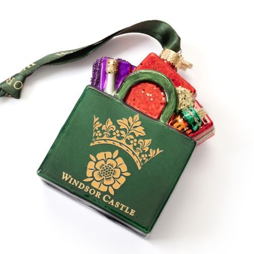 Green Glass Windsor Castle Christmas tree ornament shaped like a gift bag filled with colourful wrapped presents. The ornament features a gold crown emblem and the words "Windsor Castle” on the front. A green hanging ribbon with gold “Windsor Castle” lett