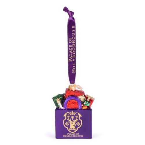 Glass Christmas ornament shaped like a purple shopping bag filled with colourful wrapped gifts. The front features the Palace of Holyroodhouse crest and gold lettering reading “PALACE OF HOLYROODHOUSE.” The ornament hangs from a purple ribbon printed with