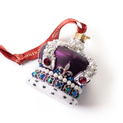 Glass Christmas ornament shaped like an ornate royal crown, finished in deep purple with silver detailing and decorated with faux pearls and multicoloured jewel accents. The crown features a white ermine-style trim with black spots and hangs from a red ri