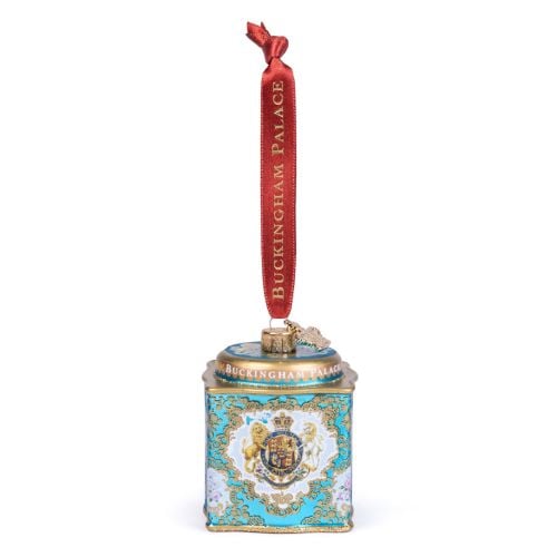 Glass Christmas ornament shaped like an ornate turquoise decorative tin, featuring the Royal Coat of Arms surrounded by intricate gold scrollwork and floral details. The lid is trimmed with gold accents and the ornament hangs from a red ribbon printed wit