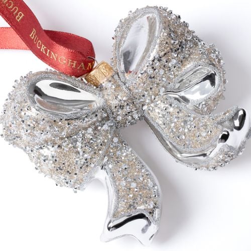 Silver glass bow decoration with glitter detailing, suspended from a red Buckingham Palace ribbon.