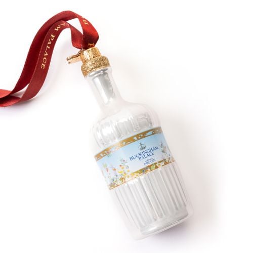 Glass Christmas ornament shaped like a pale blue Buckingham Palace Dry Gin bottle, featuring a decorative label with floral details, gold accents and the Buckingham Palace Dry Gin logo. The bottle hangs from a red ribbon printed with “BUCKINGHAM PALACE” i