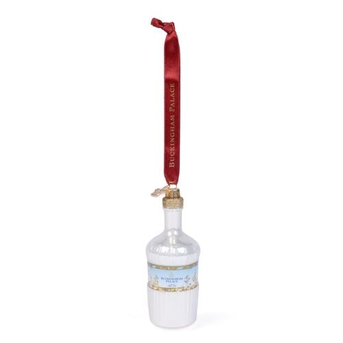 Glass Christmas ornament shaped like a pale blue Buckingham Palace Dry Gin bottle, featuring a decorative label with floral details, gold accents and the Buckingham Palace Dry Gin logo. The bottle hangs from a red ribbon printed with “BUCKINGHAM PALACE” i