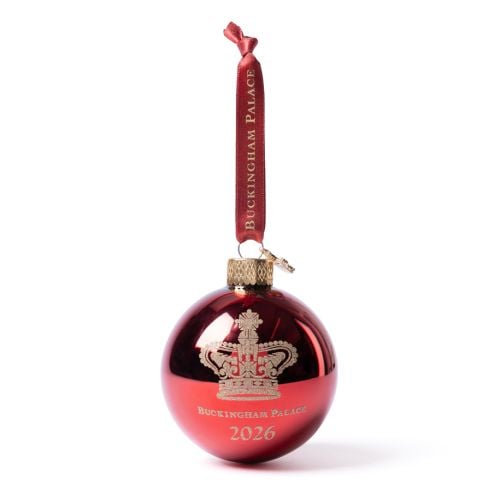 Red glass Christmas bauble with gold crown motif and ‘Buckingham Palace 2026’ engraving, finished with a red ribbon hanger which says "Buckingham Palace" in gold writing.