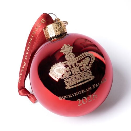 Red glass Christmas bauble with gold crown motif and ‘Buckingham Palace 2026’ engraving, finished with a red ribbon hanger which says "Buckingham Palace" in gold writing.