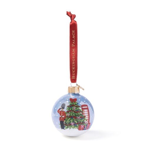 Buckingham Palace Christmas Scene glass bauble showing a decorated Christmas tree, guard figure and red telephone box with gift details, finished with a red ribbon hanger with the writing 'Buckingham Palace' in gold. 

