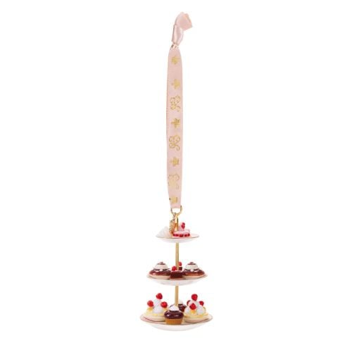 Three-tier cake stand hanging ornament featuring miniature cupcakes and iced cakes with red berry decorations on white plates. The ornament is suspended from a pale pink ribbon decorated with gold crown motifs and finished with a pink ribbon loop.