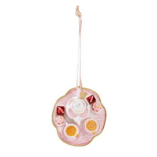 Decorative hanging ornament featuring a white and gold teapot with pink floral detailing, set on a pink serving tray with two teacups filled with tea, miniature cakes, and pink cupcakes. The ornament hangs from a pale pink ribbon decorated with gold crown