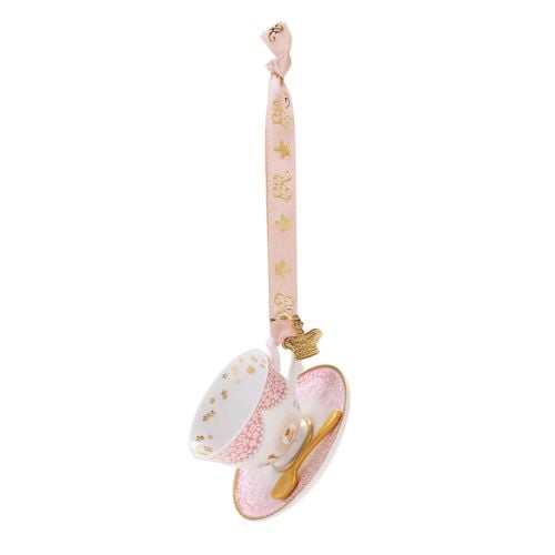Decorative hanging teacup and saucer ornament featuring a white teacup with pink floral and gold detailing, resting on a matching pink saucer. A miniature gold spoon sits on the saucer, and the ornament hangs from a pale pink ribbon decorated with gold cr