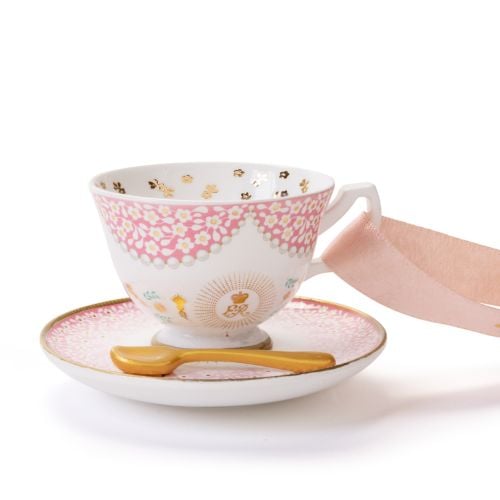 Decorative hanging teacup and saucer ornament featuring a white teacup with pink floral and gold detailing, resting on a matching pink saucer. A miniature gold spoon sits on the saucer, and the ornament hangs from a pale pink ribbon decorated with gold cr