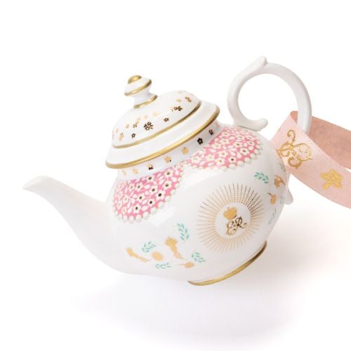 Decorative hanging teapot ornament featuring a white teapot with pink floral panels, gold accents, and delicate blue floral detailing. The ornament hangs from a pale pink ribbon decorated with gold crown motifs and includes a gold crown charm attached abo