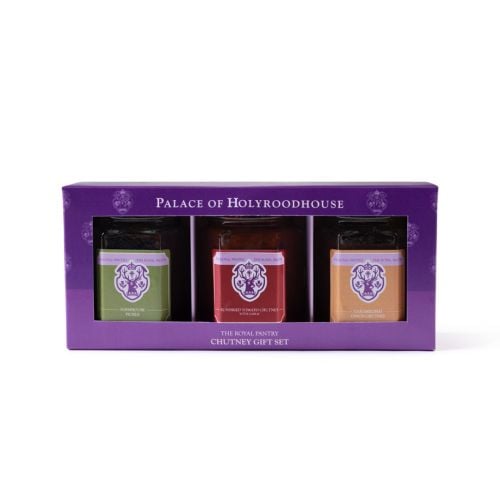 Three glass jars of The Royal Pantry condiments with black lids in a purple gift box, including Farmhouse Pickle, Sundried Tomato Chutney with Garlic, and Caramelised Onion Chutney, each featuring a distinctive coloured label and royal-inspired crest desi