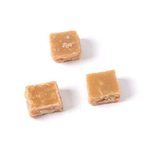 Box of Buckingham Palace Crumbly Clotted Cream Fudge from The Royal Pantry, presented in a navy blue carton with a crown motif and a clear window showing fudge pieces inside. Two cubes of golden clotted cream fudge are displayed in front of the box.
