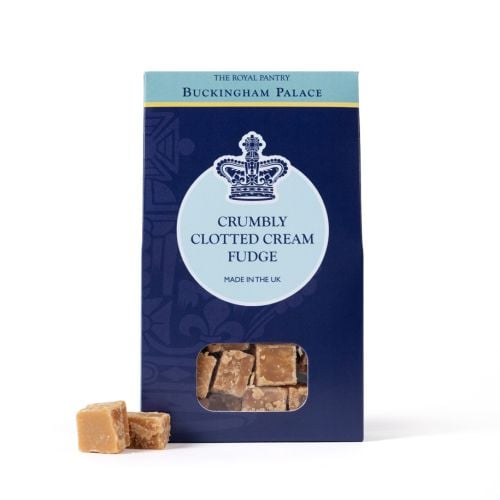 Box of Buckingham Palace Crumbly Clotted Cream Fudge from The Royal Pantry, presented in a navy blue carton with a crown motif and a clear window showing fudge pieces inside. Two cubes of golden clotted cream fudge are displayed in front of the box.