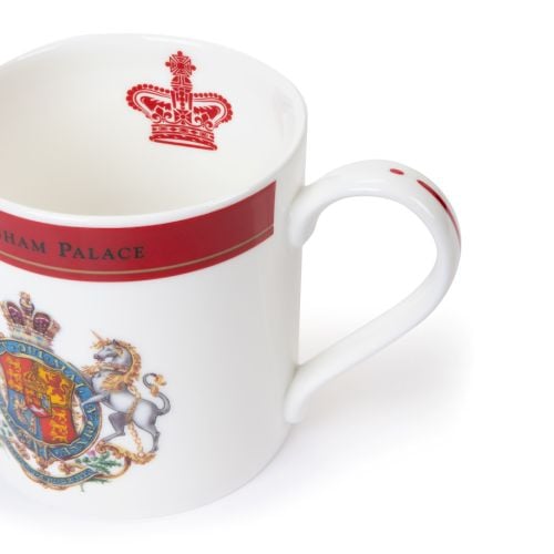 White bone china mug with a red band and gold trim reading “Buckingham Palace,” featuring a detailed Royal Coat of Arms with a lion and unicorn.