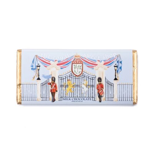 Milk chocolate bar wrapped in a pale blue sleeve illustrated with decorative gates, royal guards, and heraldic motifs, finished with gold foil ends and the text “The Royal Sweet Shop” and “Milk Chocolate – Made in the UK”.
