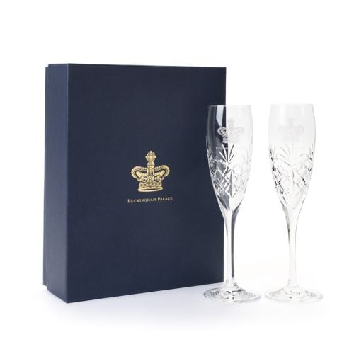 Pair of crystal champagne flutes with Buckingham Palace engraving, presented beside a navy gift box with gold crown insignia.