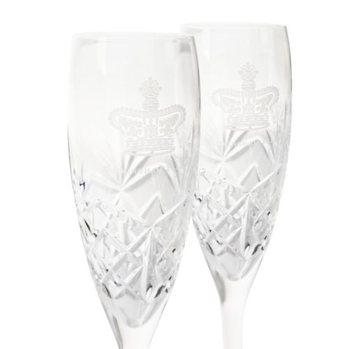 Pair of crystal champagne flutes with Buckingham Palace engraving, presented beside a navy gift box with gold crown insignia.