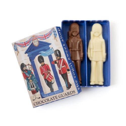 Box of “Milk and White Chocolate Guards” featuring illustrated British ceremonial guards in red uniforms and tall black hats, with a bagpiper and drummer standing beneath a blue arch decorated with Union Jack bunting. A small blue flag reads “Handmade in