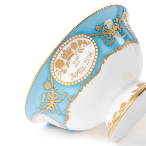 Queen Elizabeth II 90th Birthday Limited Edition Teacup and Saucer in gold and blue next to gold presentation box. 