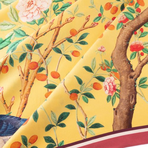 Yellow floral scarf featuring illustrated birds, flowering branches, berries and a hanging birdcage, finished with a pink border.