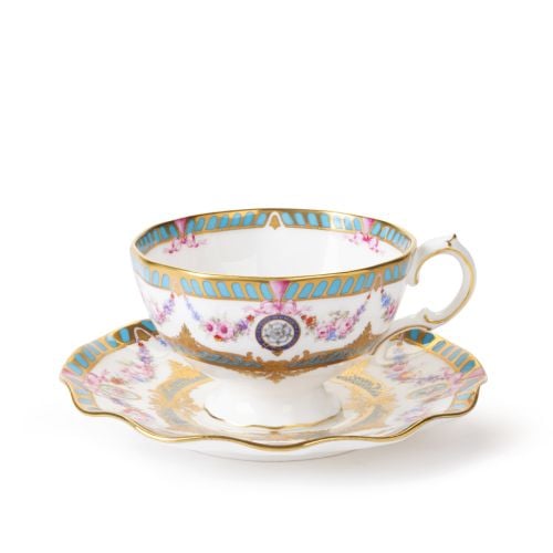 Fine bone china teacup and saucer with gold detailing, turquoise border accents, pink floral garlands and decorative medallions, viewed from above.