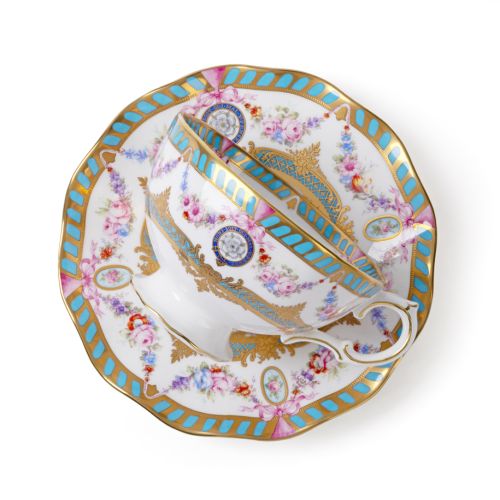 Fine bone china teacup and saucer with gold detailing, turquoise border accents, pink floral garlands and decorative medallions, viewed from above.